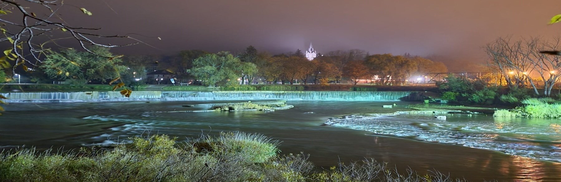 Falls and river lit up at night with surrounding trees