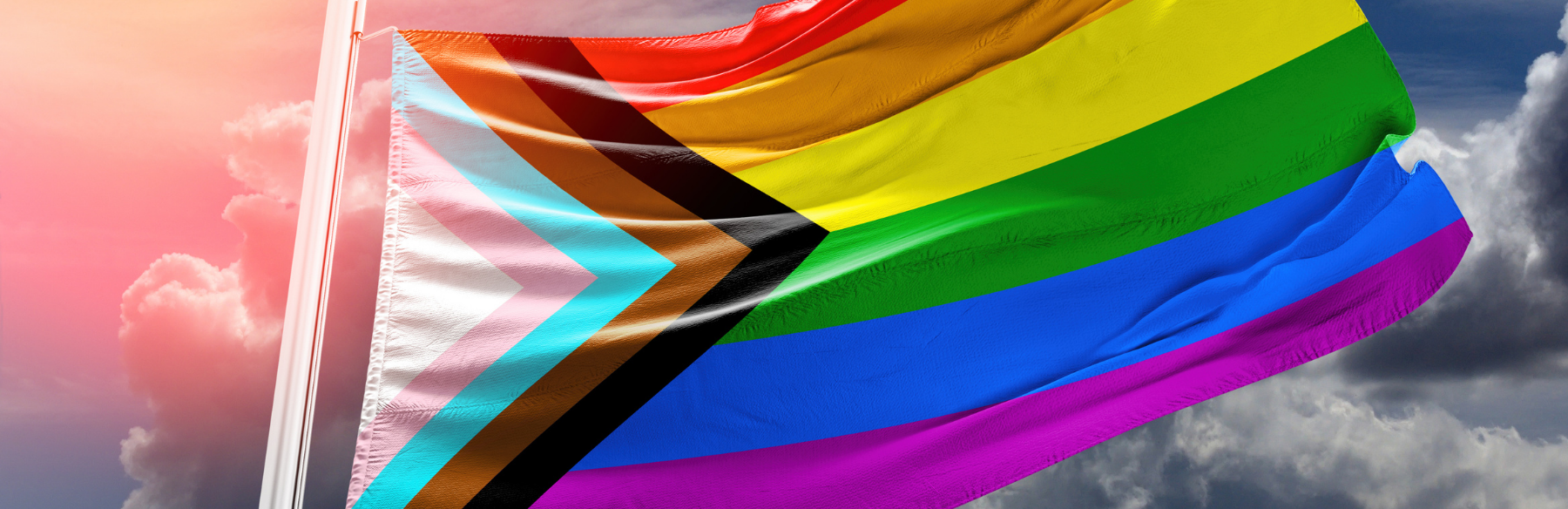 The progress pride flag flying against a blue sky.